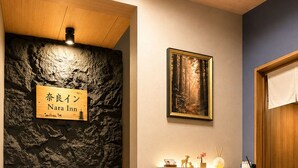 Un espace d’accueil avec un comptoir en bois, une enseigne fixée au mur indiquant « Nara Inn », et un tableau encadré au-dessus du comptoir.