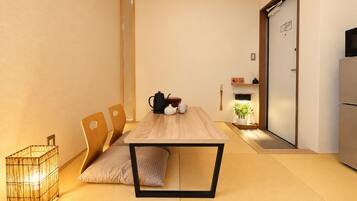 Quarto minimalista com mesa de jantar de madeira, cadeiras, pequena área de cozinha e porta deslizante.