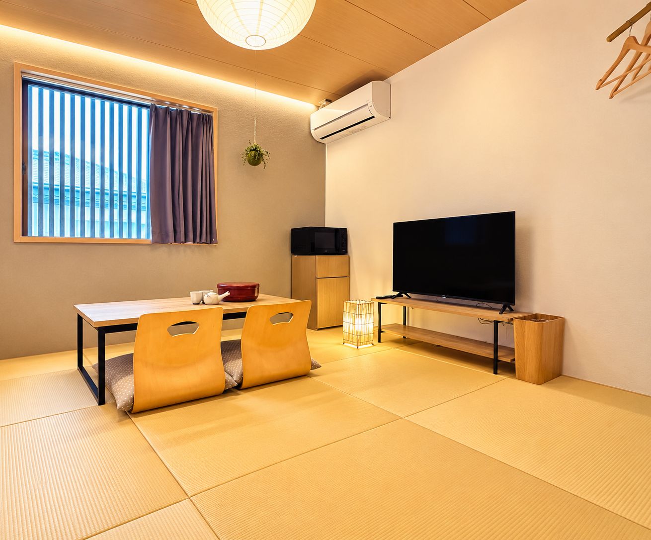 Quarto com piso de tatame, televisão, mini-geladeira e janela com persianas.