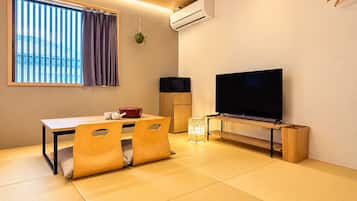 Quarto com piso de tatame, televisão, mini-geladeira e janela com persianas.