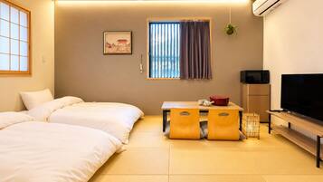 A hotel room with two beds, a television, a small table with a red pot, and a window with curtains.