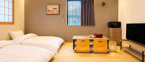 A hotel room with two beds, a television, a small table with a red pot, and a window with curtains.