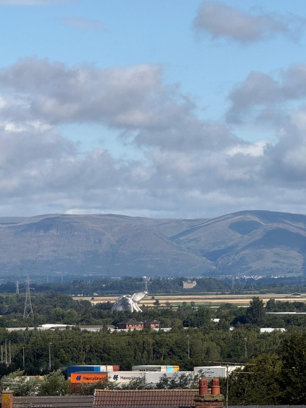 Een landschap met bergen, een windmolen en industriële gebouwen.