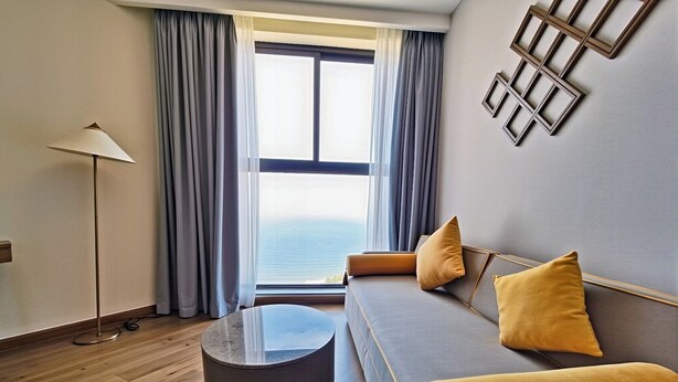 A modern living room with a sofa, round ottoman, and a floor lamp. - Mandala Coast Luxury Hotel (Mui Ne)