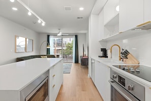 Une cuisine moderne avec des meubles blancs, un îlot central, un four encastré et un coin repas offrant une vue agréable.