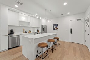 Une cuisine moderne avec des meubles blancs, un lave-vaisselle en acier inoxydable, un réfrigérateur et un îlot central doté de tabourets.