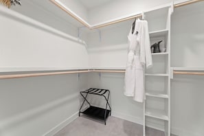 A walk-in closet with a hanging rack, shelves, and a shoe rack. - Chic South Lamar | Pool, Restaurant, Bar, Terrace, Creative Space | The Code (Austin)