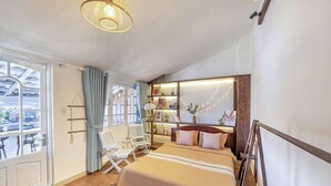 Ein Hotelzimmer mit einem großen Bett, einer Sitzecke mit Sesseln, einem Bücherregal und Blick ins Freie.