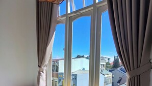Ein Zimmer mit großem Fenster, einem Bett mit Holz-Kopfschild und einer Pendelleuchte.