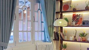 Ein Zimmer mit zwei weißen Schaukelstühlen, Holzboden, einem fenster mit Vorhängen und einem Regal mit Dekoration.