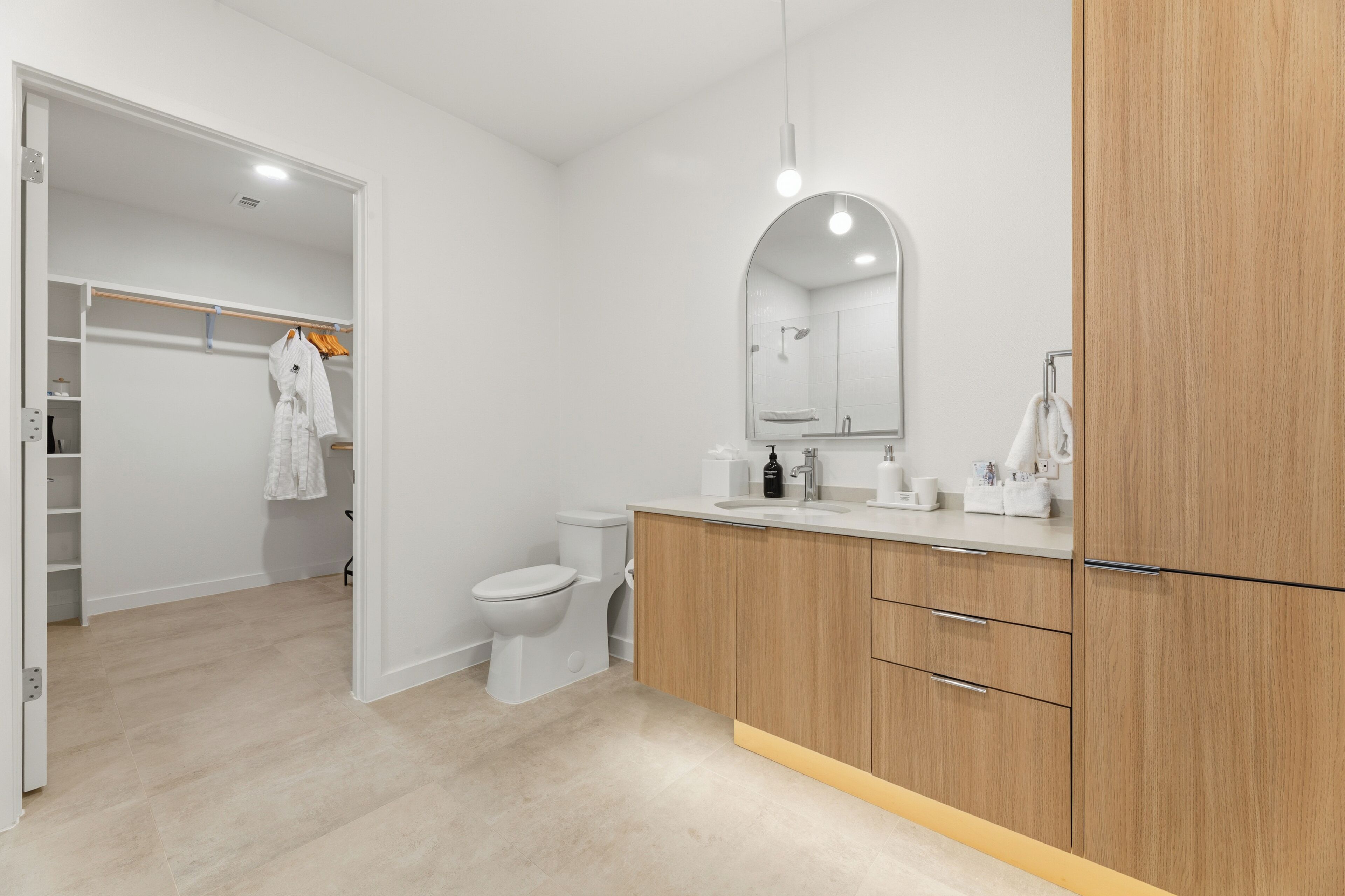 A modern bathroom with a toilet, sink, mirror, and wooden cabinets.