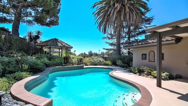 A swimming pool with a curved edge, surrounded by a brick deck and lush greenery. - Grand House in Mt. Helix (El Cajon)