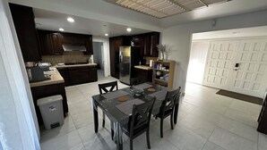 A modern kitchen with dark wood cabinets, a stainless steel refrigerator, and a dining area with a table and chairs. - Grand House in Mt. Helix (El Cajon)