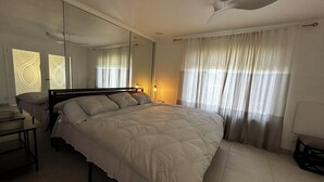 A bedroom with a large bed, a ceiling fan, a nightstand, a desk, and a mirror. - Grand House in Mt. Helix (El Cajon)