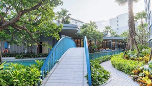 Un camino conduce a una zona de piscina con barandilla azul, rodeada de exuberante vegetación y palmeras.