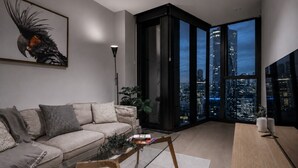 En moderne stue med sofa, sofabord og udsigt over byen gennem store vinduer.