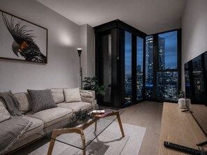 A modern living room with a sofa, coffee table, and a city view through large windows. - Skyline Suites | Stunning City Views, Gym & Pool (Southbank)