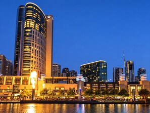 A city skyline with modern high-rise buildings, a waterfront, and a well-lit public space. - Skyline Suites | Stunning City Views, Gym & Pool (Southbank)