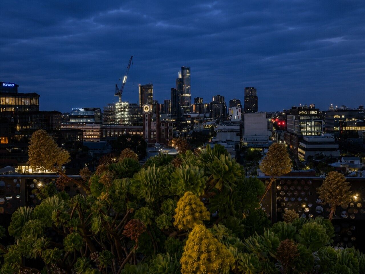 Horizonte urbano al atardecer con edificios iluminados y grúas de construcción.