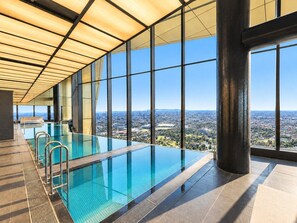 A modern indoor swimming pool with clear glass walls, offering a city view. - Skyline Suites | Cosy Study Suite, Australia 108 (Southbank)