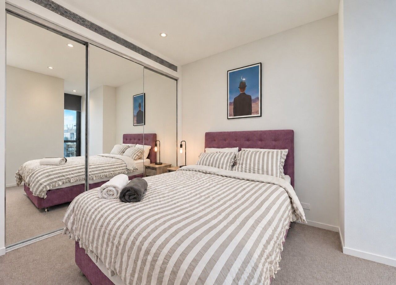 A bedroom with two beds, a large mirror, and a framed picture on the wall.