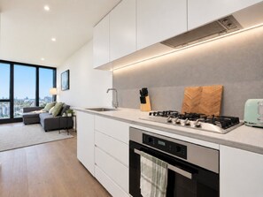 A modern kitchen with a gas stove, built-in oven, and a large window offering a city view. - Skyline Suites | Cosy Study Suite, Australia 108 (Southbank)