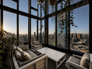 A modern room with large windows, a sofa, a table, and hanging plants. - Skyline Suites | Cosy Study Suite, Australia 108 (Southbank)