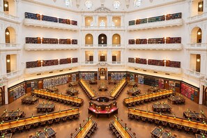 Une bibliothèque à plusieurs niveaux, dotée de nombreuses étagères, de tables de lecture et d’un escalier central.