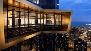 Een hoog gebouw met een glazen gevel, een balkon met zitplaatsen en uitzicht op de stad.