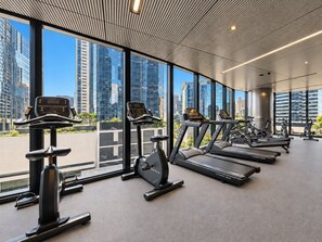 Une salle de sport équipée de matériel d’exercice et dotée de grandes fenêtres offrant une vue sur la ville.
