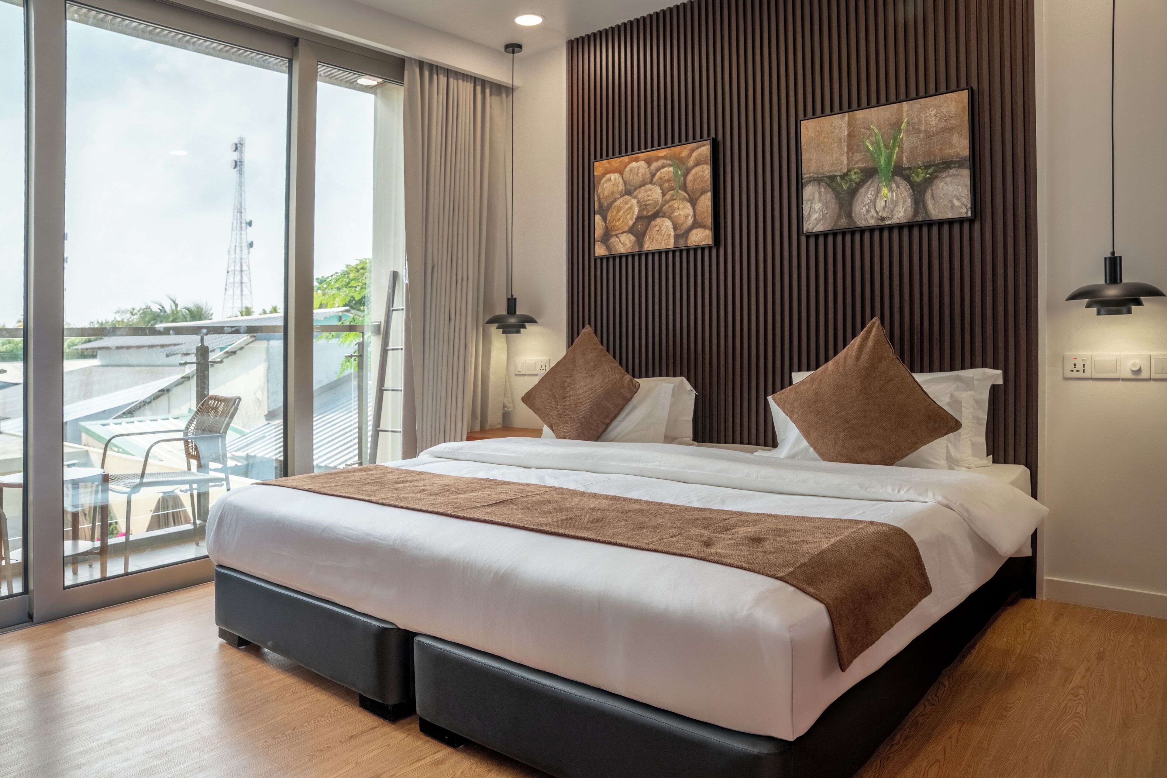A modern hotel room with a large bed, a balcony with a view, and two artworks on the wall.