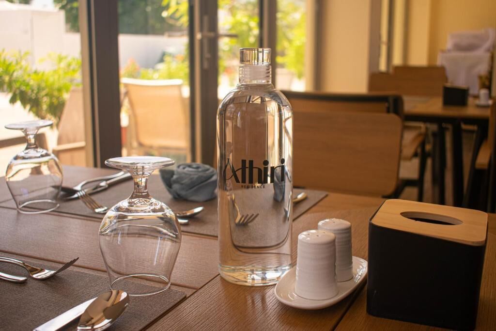 Una mesa de comedor con una botella de agua, salero, dispensador de servilletas y cubiertos.