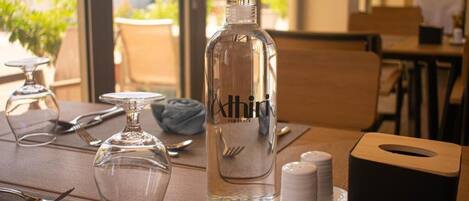 Una mesa de comedor con una botella de agua, salero, dispensador de servilletas y cubiertos.