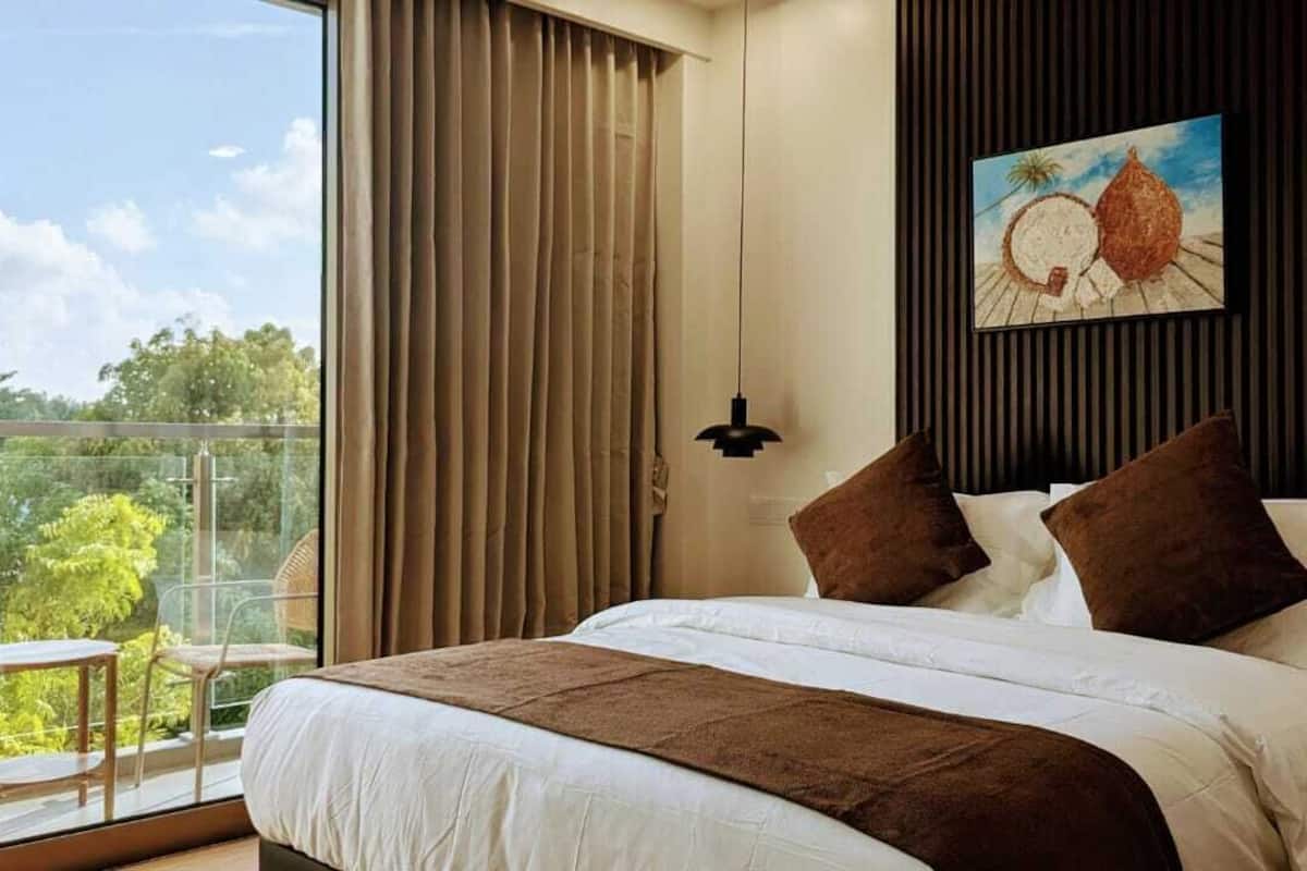 A bedroom with a large bed, a view of greenery outside, and a painting on the wall.