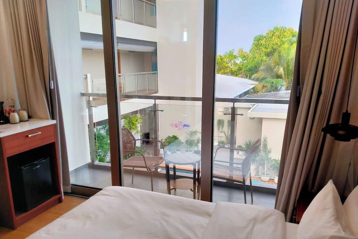 A hotel room with a large balcony, a bed, a desk with a chair, and a view of the outside balcony area.