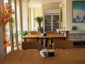 A dining area with a wooden table and chairs, a potted plant, a refrigerator, and a painting on the wall.
