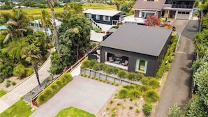 A modern house with a large patio, surrounded by lush greenery and a view of the sea. - Up Above The Crescent (Waihi Beach)