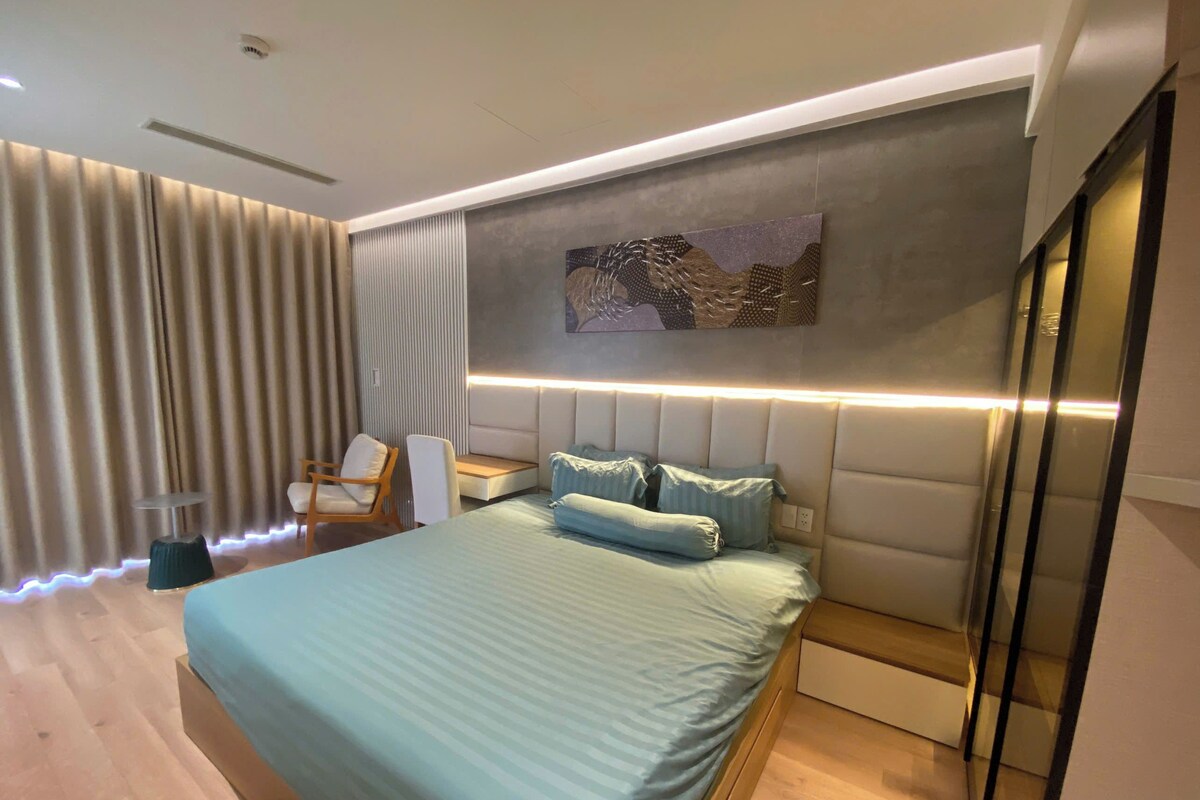 A modern bedroom with a bed, bedside table, and a seating area with a chair and a small table.