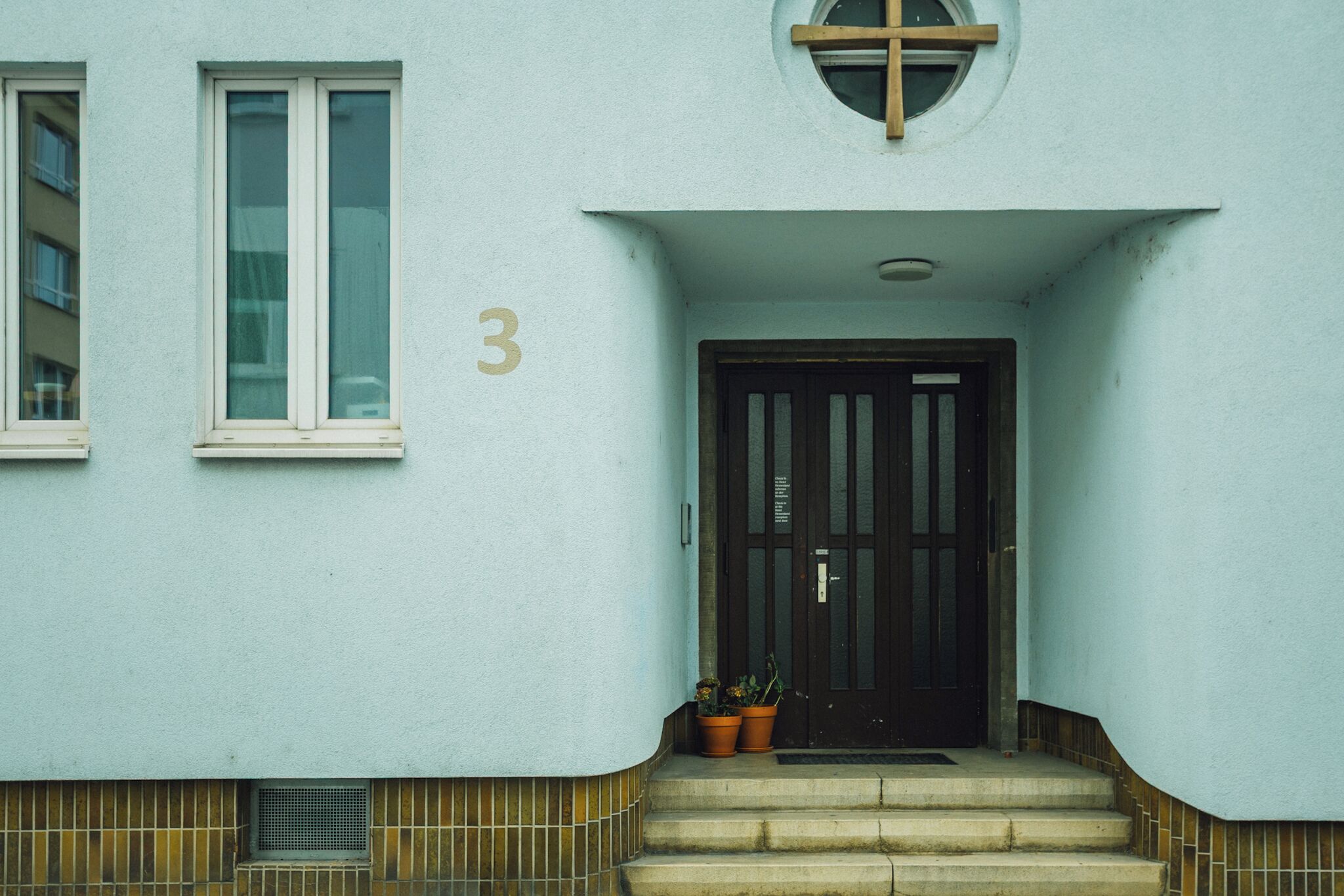 Ein Gebäude mit hellblauer Fassade, einer schwarzen Tür und der Zahl 3 an der Wand.