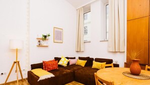 Ein gemütliches Wohnzimmer mit einer braunen Eckcouch, einem runden Holzesstisch und einem weißen Teppich.