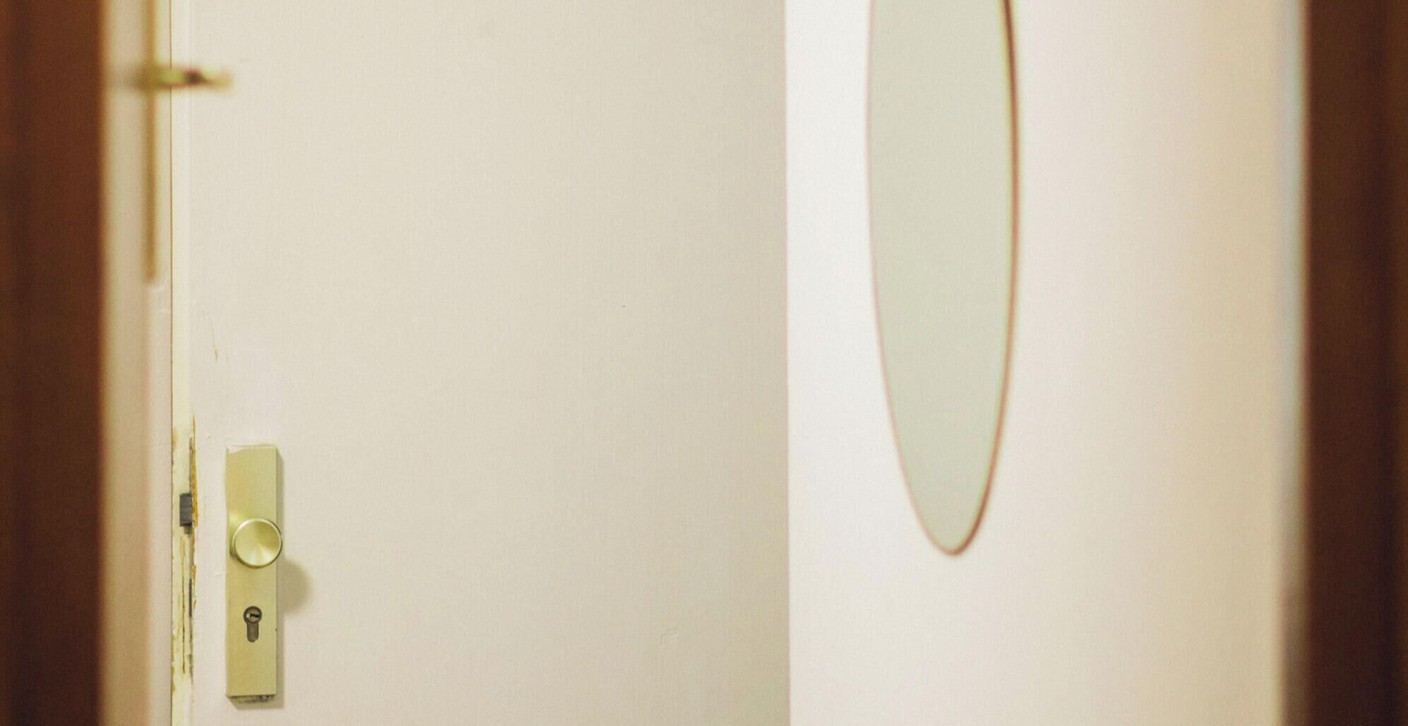 A door with a keyhole and a handle, and a mirror on the wall.