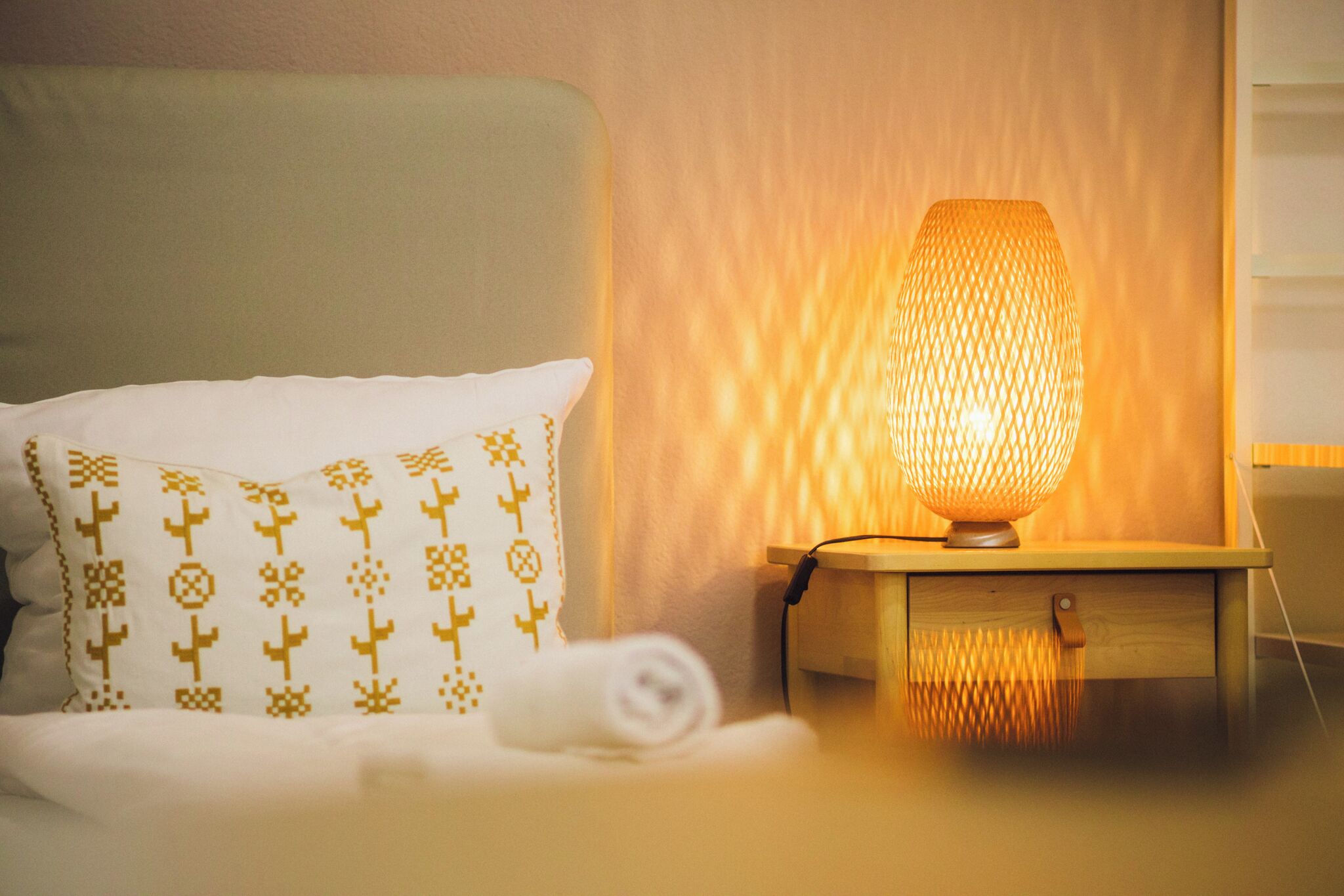 A neatly made bed with a patterned pillow and a bedside table with a textured lamp.