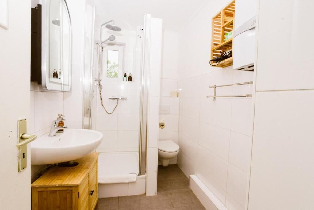 Un baño con lavamanos blanco, cabina de ducha de vidrio, inodoro y armario de madera.