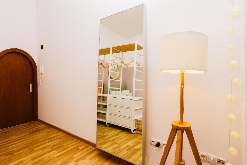 Una habitación con suelo de madera, una puerta de madera, un armario blanco con estantes y una lámpara de pie.