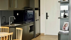 Une cuisine moderne avec des meubles de couleur sombre, un plan de travail noir et un four encastré. On y trouve une table à manger en bois avec des chaises.
