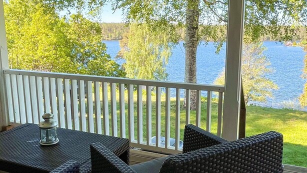 Un espace extérieur aménagé, abrité et doté de meubles en osier et d’une lanterne, offrant une vue sur un lac.