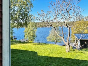 Blick auf einen See mit einer Wiese, einem Baum und einem kleinen Gebäude mit Dach.