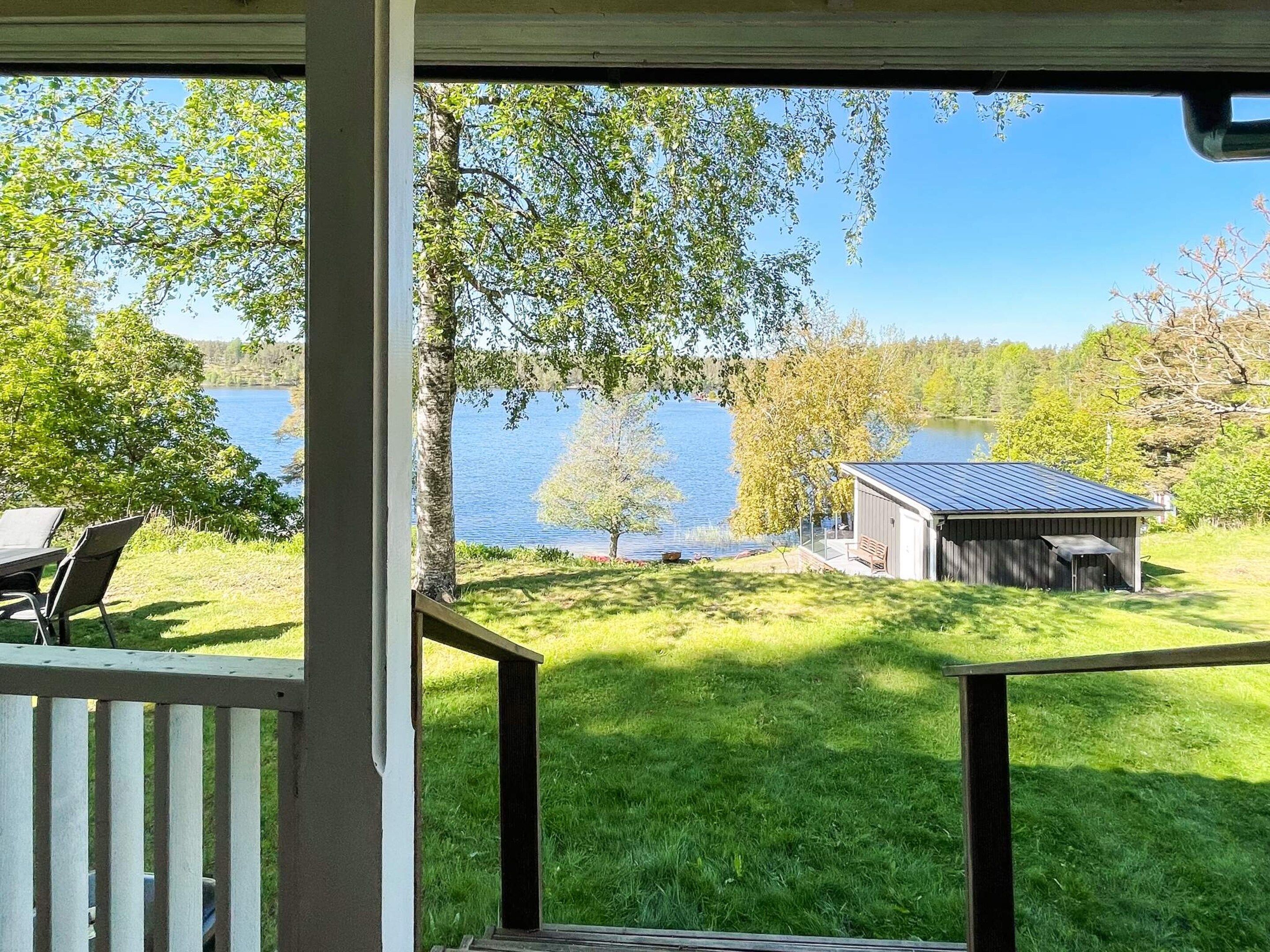 A covered outdoor area with a view of a lake, a small shed, and a grassy lawn.