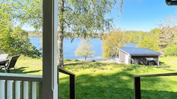 A covered outdoor area with a view of a lake, a small shed, and a grassy lawn.