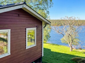 A wooden cabin with two windows, a grassy yard, and a lake view. - 4 Star Holiday Home in Gamleby (Gamleby)